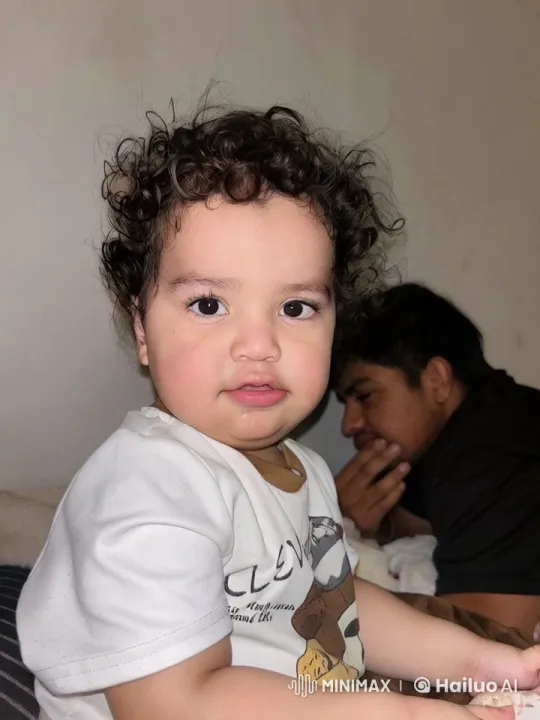 Child with Curly Hair Plays on Bed with Another Person – AI Generated Video | Hailuo AI