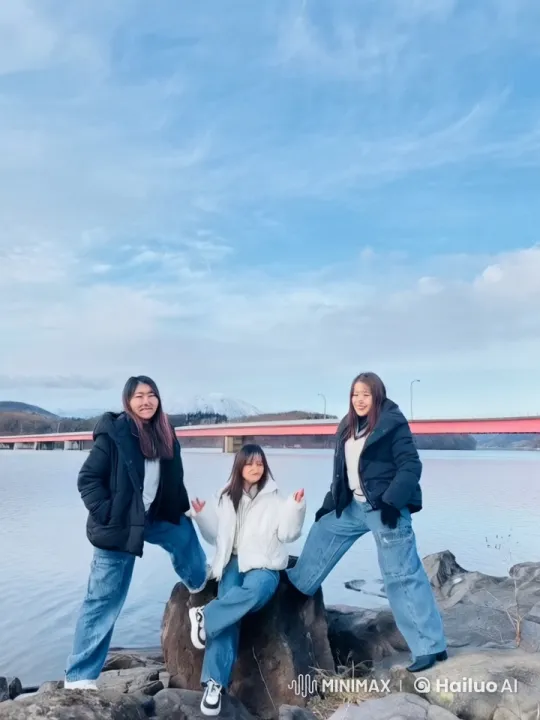 Three Friends Playfully Interact by Lake with Red Bridge – AI Generated Video | Hailuo AI