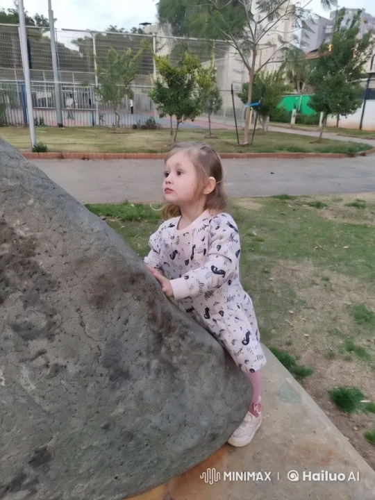 Girl in Pink Explores Park Rock Amid Urban Nature – AI Generated Video | Hailuo AI