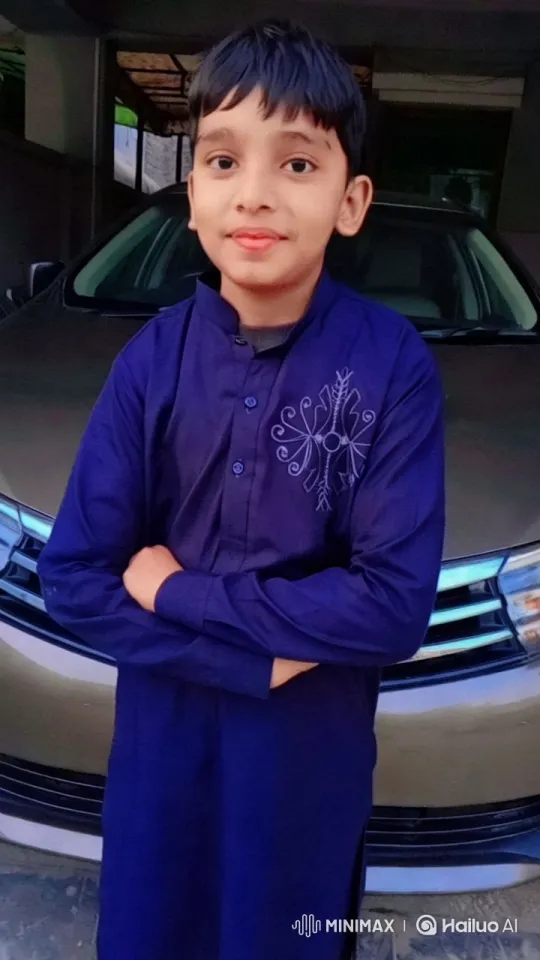 Boy in Blue Stands confidently in front of a parked car, wearing a dark blue traditional outfit with intricate embroidery on the chest. His arms are crossed, striking a relaxed yet poised posture. The background reveals a garage setting, with visible structures and hints of greenery through the windows. The camera quickly moves to the right, capturing the boy's stance and the car's sleek design from a new angle. At the same time, a tracking shot follows the boy's subtle movements, ensuring he remains the focal point of the scene. The entire video maintains a high aesthetic style, emphasizing the contrast between the boy's deep blue outfit and the soft tones of the car and surrounding environment. – AI Generated Video | Hailuo AI