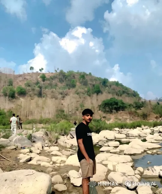 Young Man on Rocky Riverbank with Lush Hills – AI Generated Video | Hailuo AI