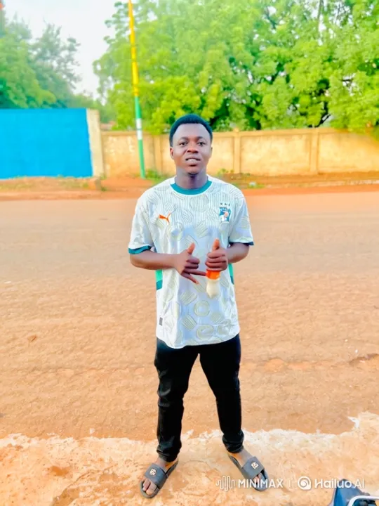 Young Man Enters Lamborghini旁白: The video begins with a full shot of a young man standing on a dirt-covered roadside, looking directly at the camera. He is dressed in a white and green patterned jersey, black trousers, and slides. In the background, lush – AI Generated Video | Hailuo AI