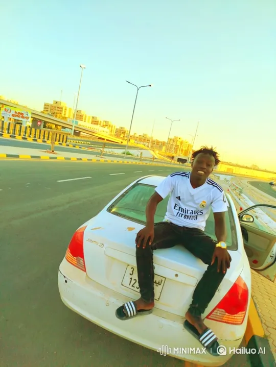 Young Black Man Smiles on Car Trunk in City Landscape – AI Generated Video | Hailuo AI