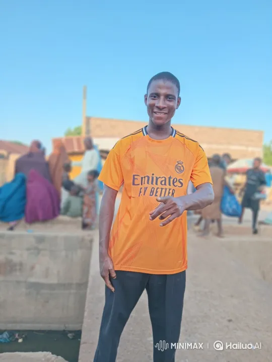 Young Man in Orange Jersey Moves with Camera in Outdoor Village – AI Generated Video | Hailuo AI