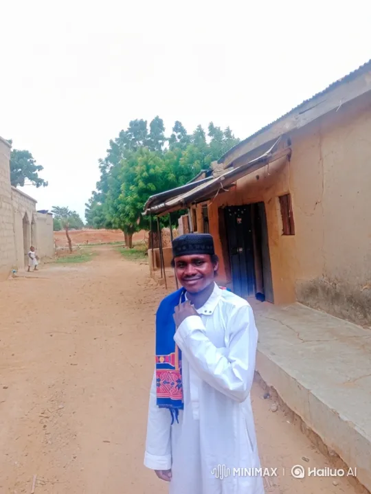 Young Man in Robe Smiles Warmly on Rural Village Path – AI Generated Video | Hailuo AI