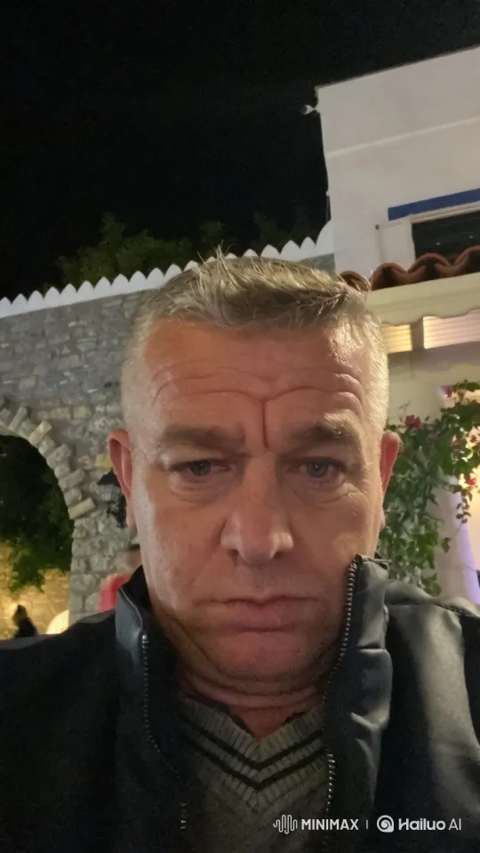 Middle-aged man with graying hair, lying on a stretcher, is carried by two paramedics into an ambulance at night, illuminated by flashing lights. – AI Generated Video | Hailuo AI